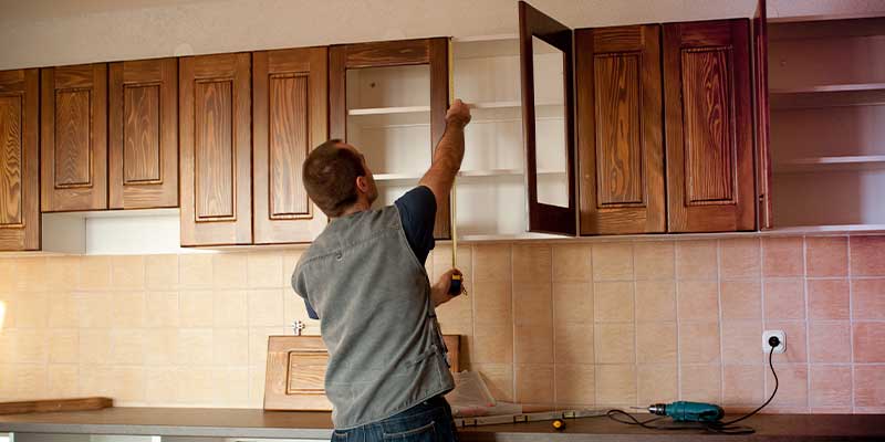 man measuring kitchen cabinets for refacing